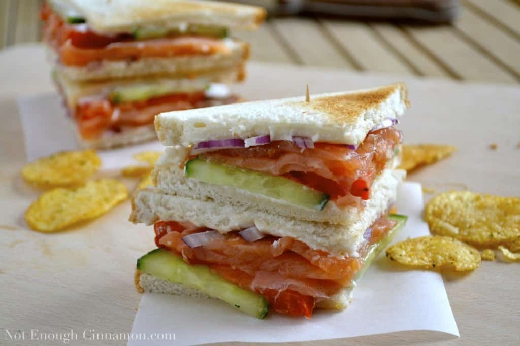 two smoked salmon club sandwiches stacked on top of each other with a toothpick, served on napkins with some potato chips on the side