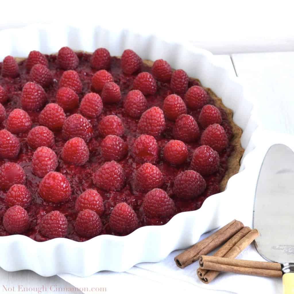 Skinny Raspberry Tart on whole wheat cinnamon crust in a white tart dish with some cinnamon sticks on the side