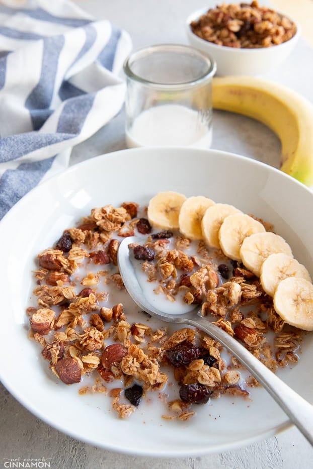 Granola is a white bowl with milk and sliced banana, with a silver spoon