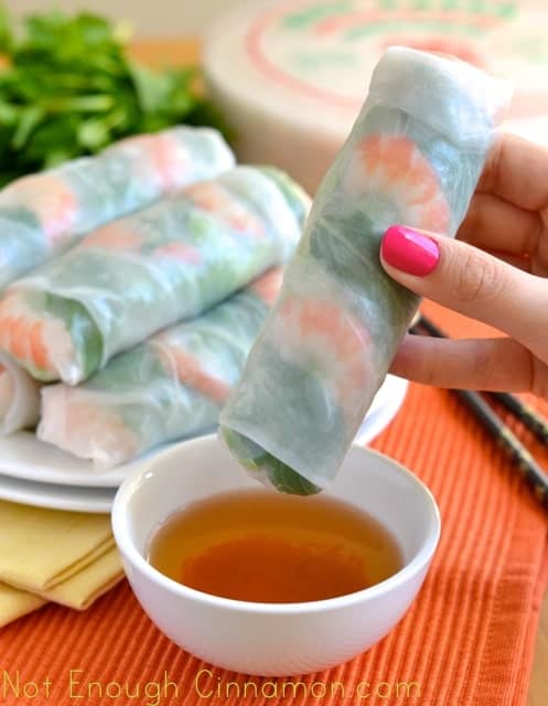 Vietnamese Spring Rolls being dipped into a small dish with dipping sauce with a plate full of spring rolls in the background