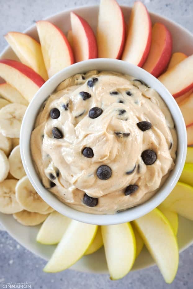 A small bowl of peanut butter chocolate chips fruit dips over a plate a cut fruits