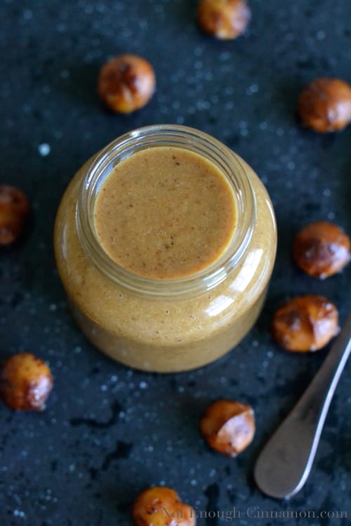 overhead shot of Paleo Honey Roasted Macadamia Nut Butter in a glass jar with some roasted macadamias surrounding it