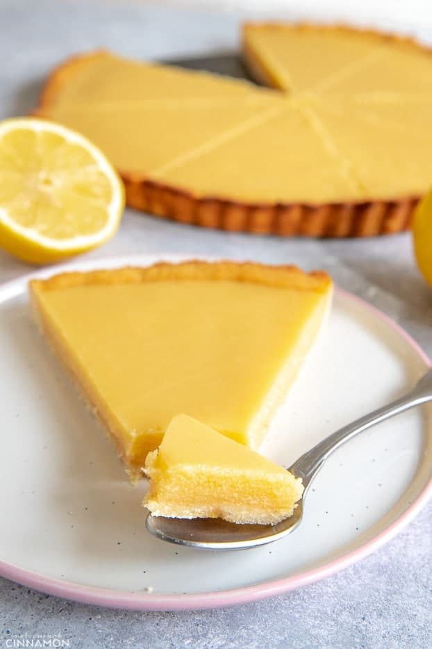 A piece of lemon curd tart in a silver spoon next to its slice.