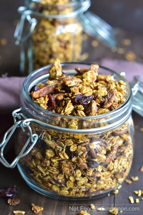 side view of a mason jar filled to the top with homemade pumpkin granola with some pecans and cranberries on top