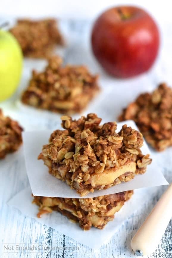 Healthy Apple Pie Oatmeal Bars with a crunchy oatmeal streusel topping stacked on top of each other with some apples and more oatmeal bars in the background