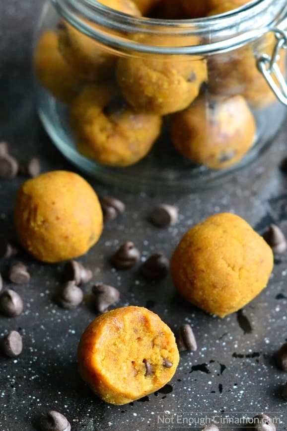 paleo pumpkin pie energy balls scattered on a black tabletop with some chocolate chips scattered in between