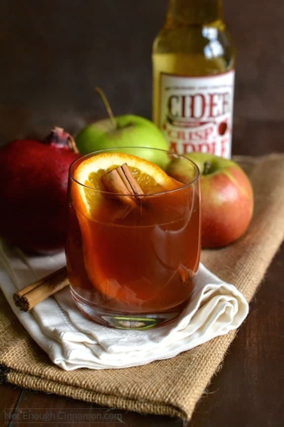 a glass of pomegranate spiced apple cider served with a cinnamon stick and orange slice in it