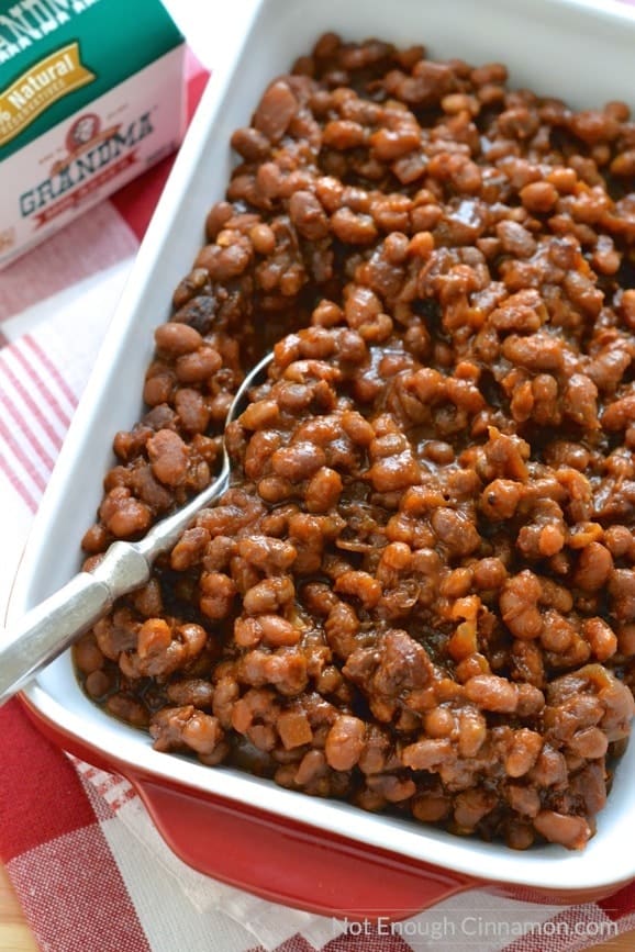 Homemade slow cooker baked beans with molasses and bacon in a red casserole dish 
