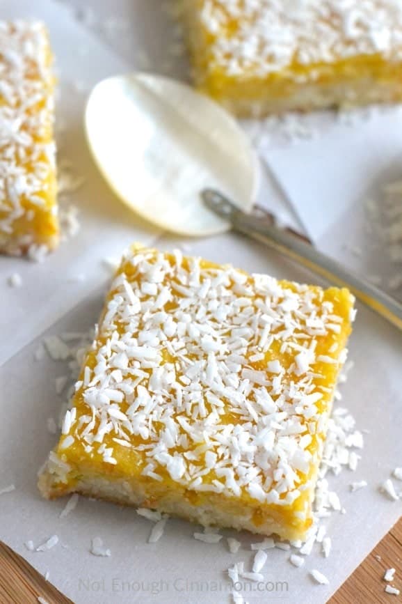 Paleo Coconut Bars with Orange Curd arranged on parchment paper with shredded coconut sprinkled on top 
