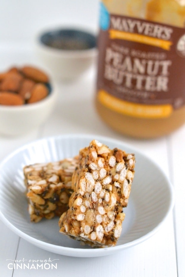two Clean Eating Peanut Butter Rice Crispy Treats on a small white saucer with a jar of peanut butter in the back