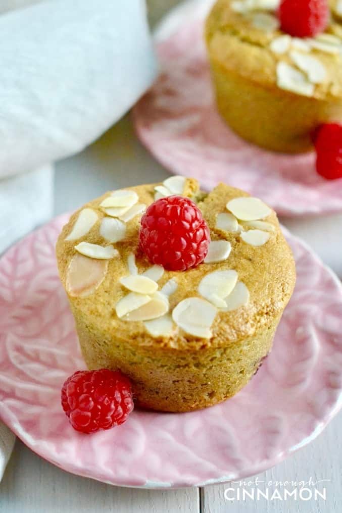 two healthy raspberry almond muffins on small pink plates topped with fresh raspberries