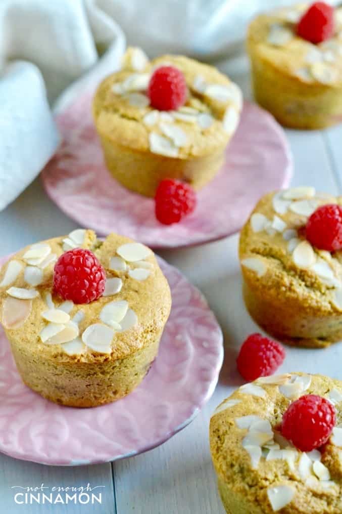 side view of raspberry almond flour muffins on pink plates topped with almonds and raspberries