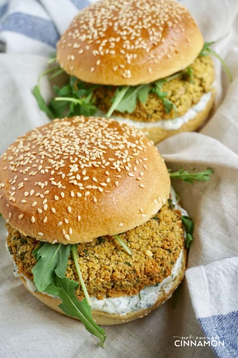 side view of two falafel burgers with falafel patties, fresh arugula and tzatziki sauce