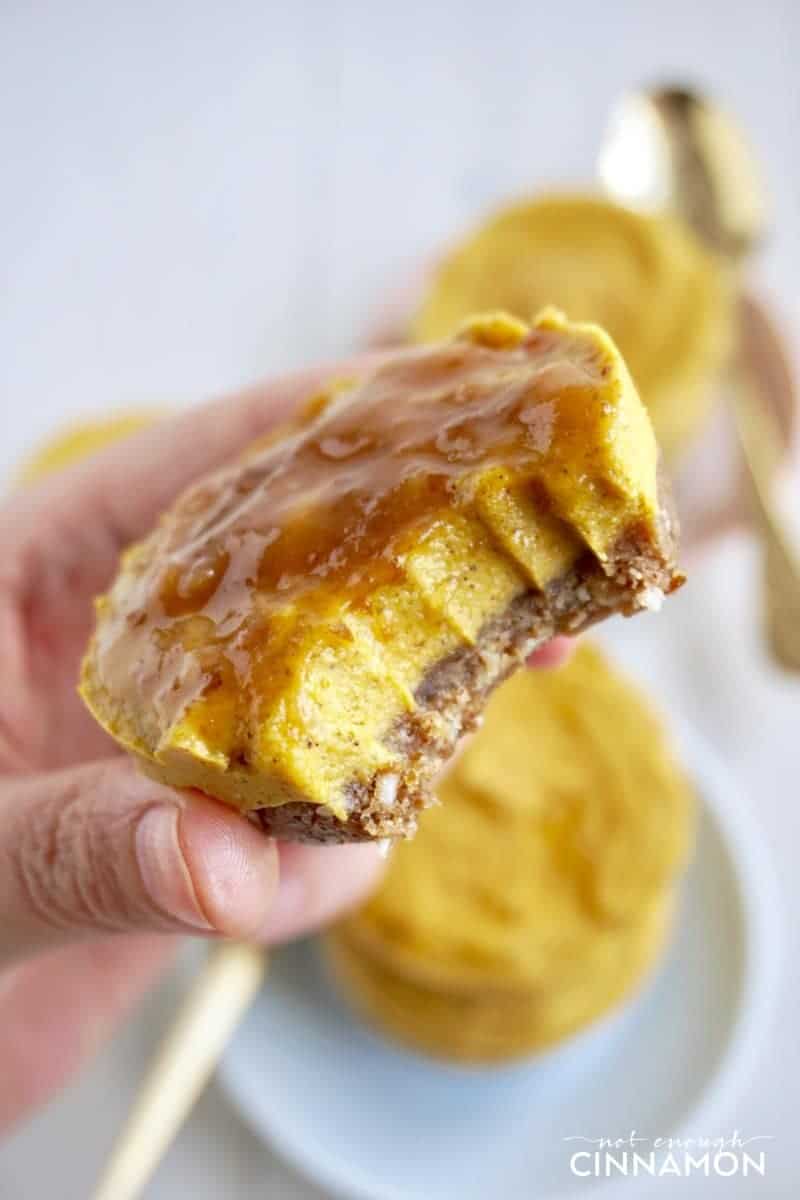 a hand holding a bite-sized vegan pumpkin cheesecake with caramel topping 