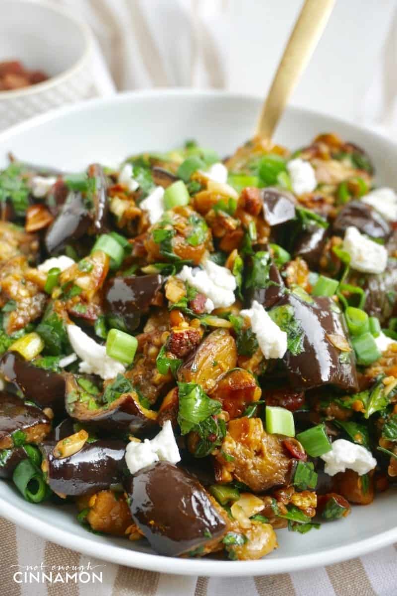close-up of roasted eggplant salad with goat cheese and smoked almonds in a white bowl