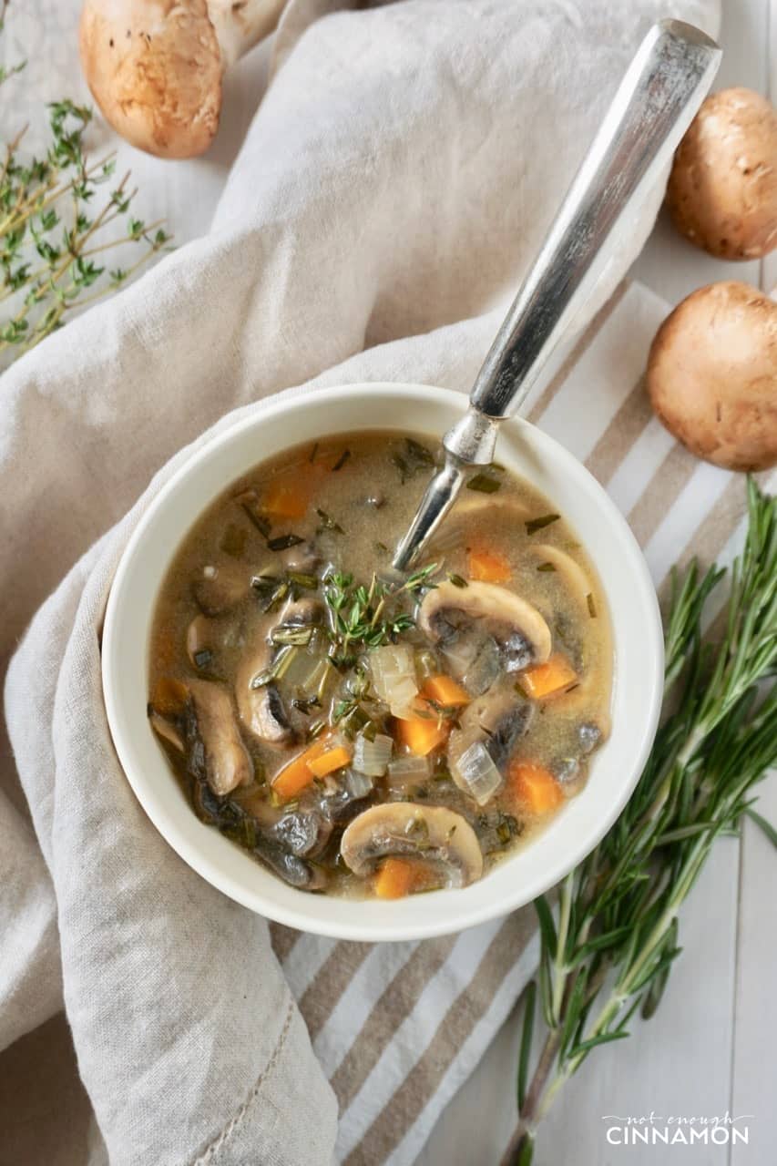 a bowl of creamy mushroom and rice soup with a twig of fresh rosemary on the side
