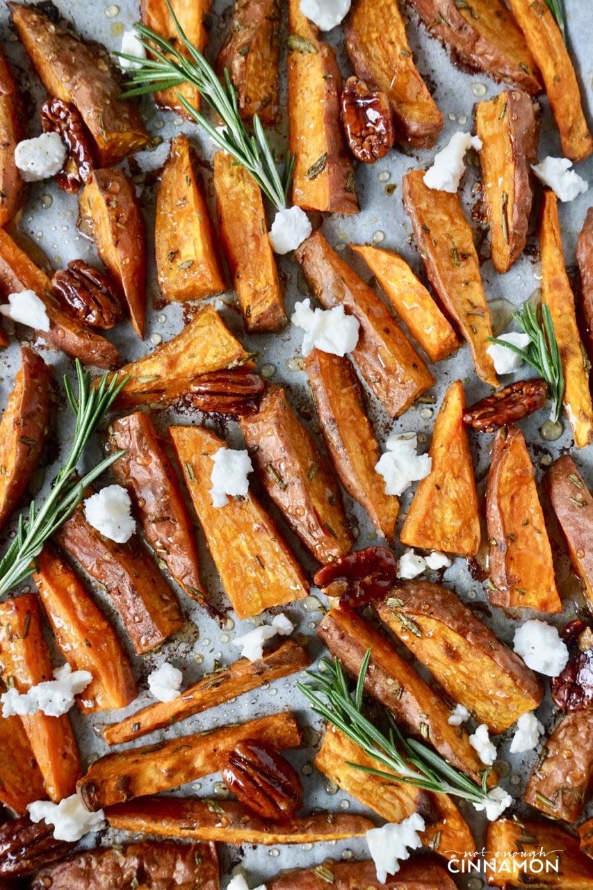 overhead shot of Sweet potato wedges on a baking sheet drizzled with olive oil, goat cheese and candied pecans 