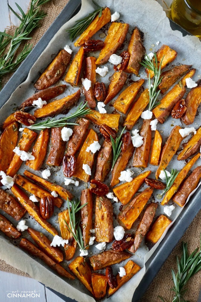 overhead shot of Sweet potato wedges on a baking sheet drizzled with olive oil and sprinkled with goat cheese and candied pecans 