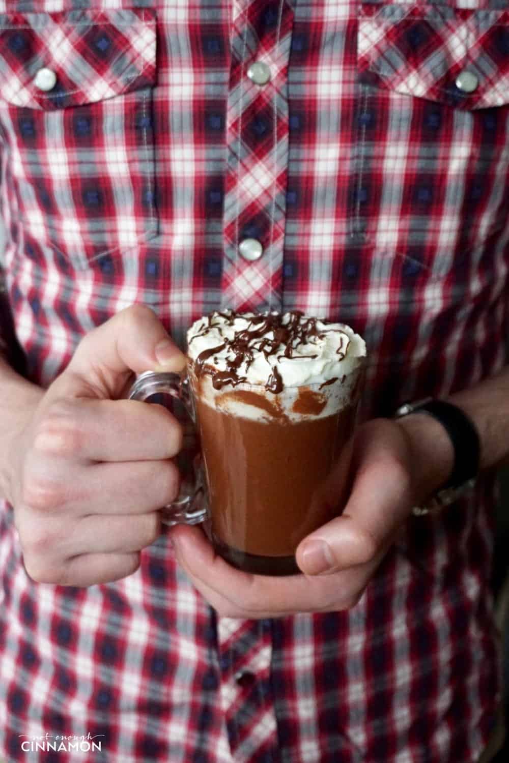 a man in a lumberjack shirt holding a mug of peanut butter hot chocolate