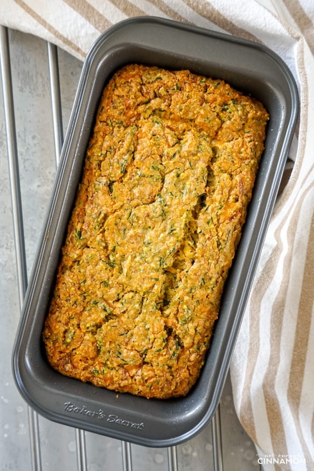 Overhead shot of a cheddar chive zucchini bread in a metal pan, right out of the oven on a metallic grill. 