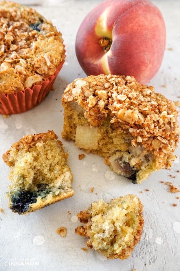 A peach and blueberry muffin torn into a few pieces to show the fruit pieces on the inside.