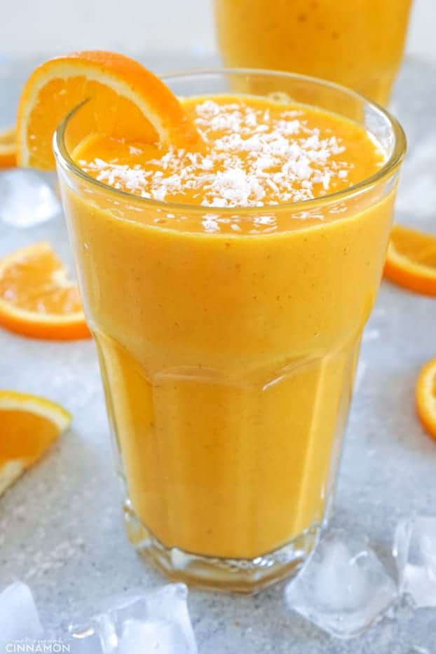 A tall glass of sunshine smoothie with shaved coconut and an orange half wheel