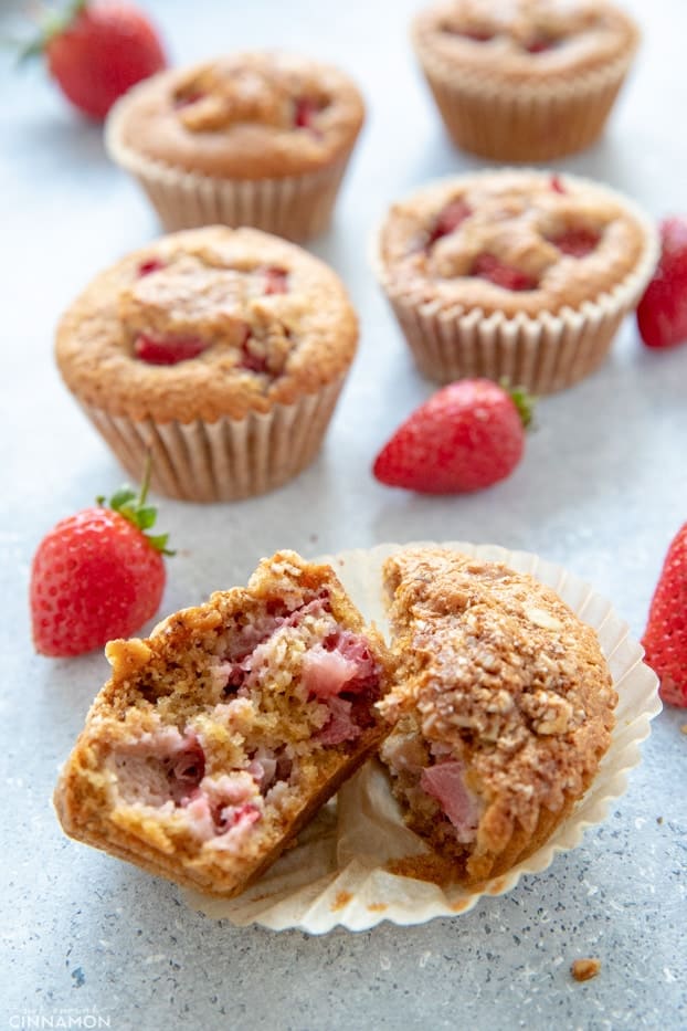 Strawberry muffin cut in half, with other muffins and strawberries around