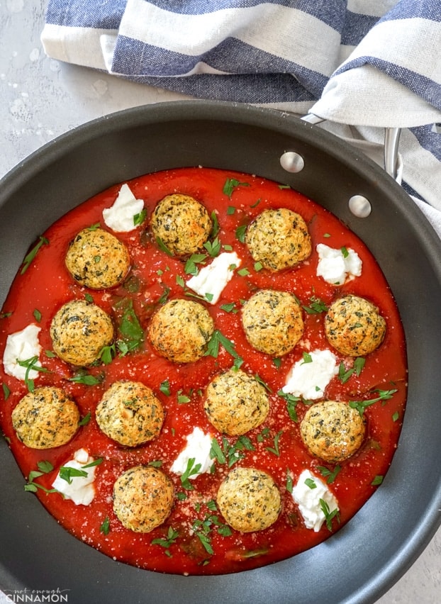 Zucchini meatballs with marinara sauce in a skillet, with a stripped kitchen towel