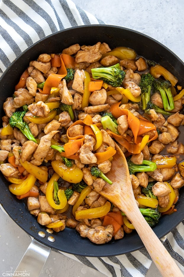overhead shot of a skillet with Chinese 5-Spice Chicken being stirred with a wooden spoon