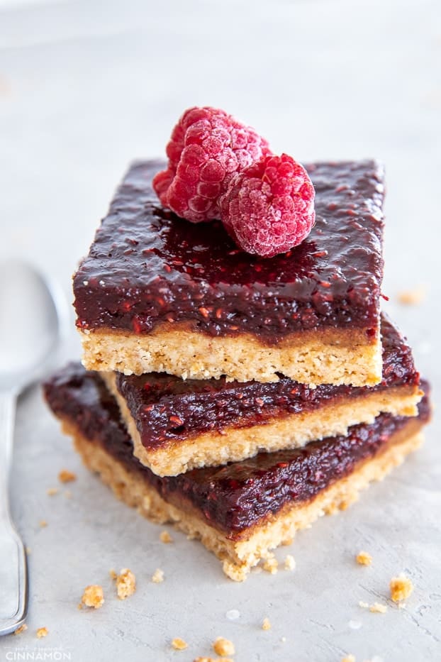 three stacked healthy raspberry almond butter bars with some crumbs on the side