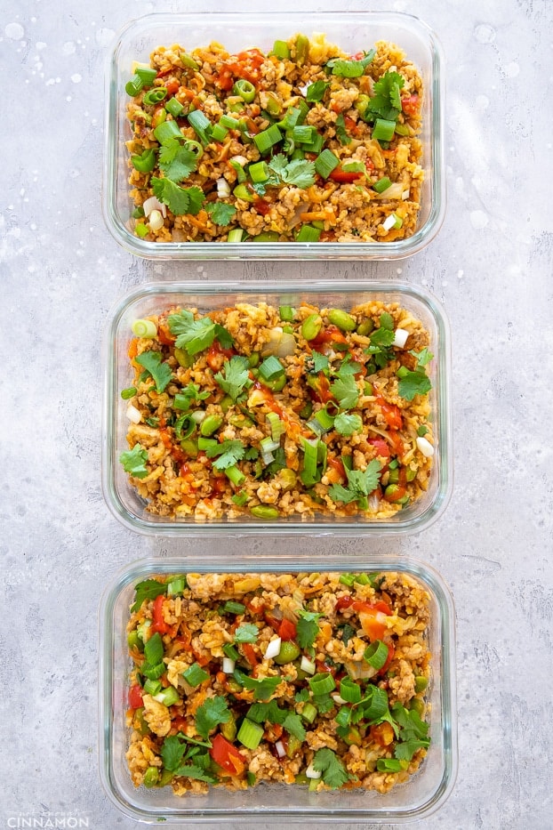 overhead shot of three glass containers with Asian Ground Turkey Fried Rice sprinkled with cilantro and sriracha sauce