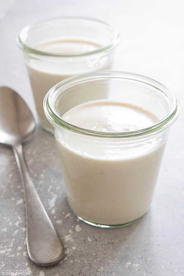 two small glasses with vegan cashew cream with a spoon on the side