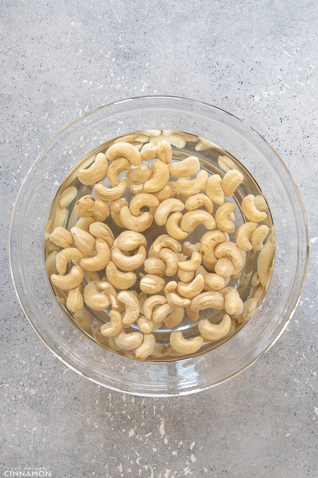 overhead shot of a big glass bowl with raw cashew nuts soaking in cold water