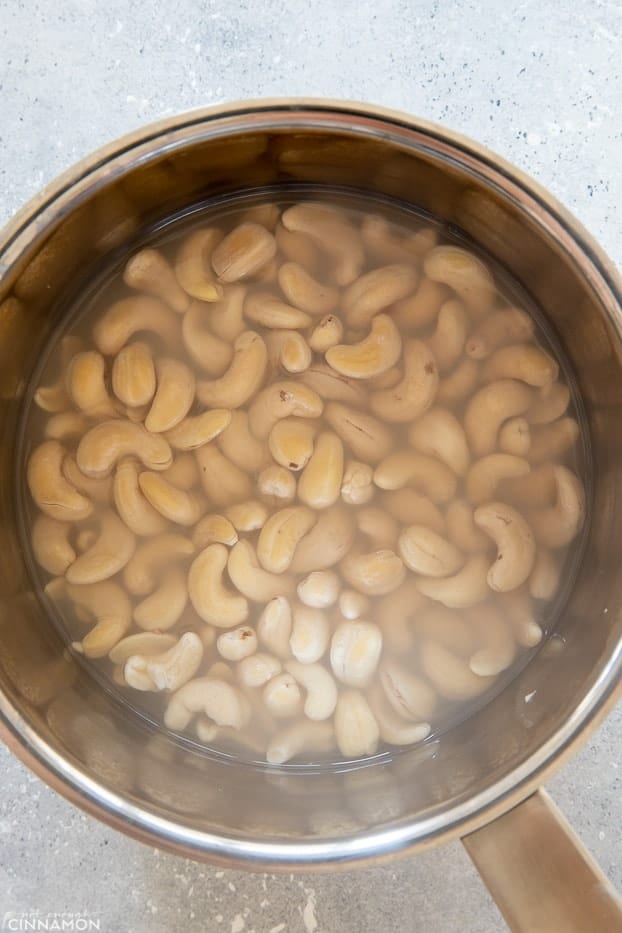 overhead shot of cashew nuts soaking in hot water in a sliver pot