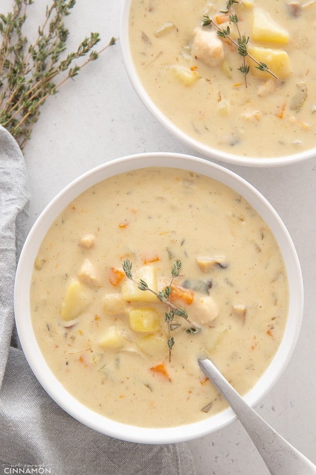 overhead shot of two white soup bowls with healthy chicken pot pie soup with fresh thyme on the side