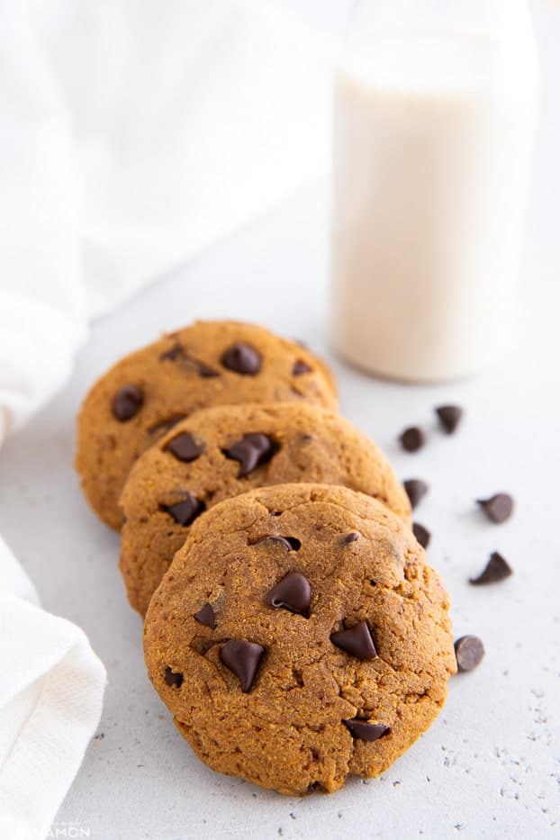 three healthy protein cookies with chocolate chips and a glass of milk in the background
