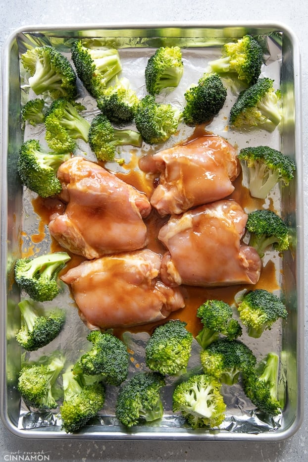 raw Teriyaki glazed chicken thighs surrounded with broccoli florets on a baking pan