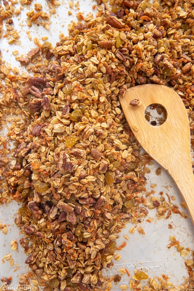 overhead shot of a sheet pan with healthy carrot granola being stirred with a wooden spoon