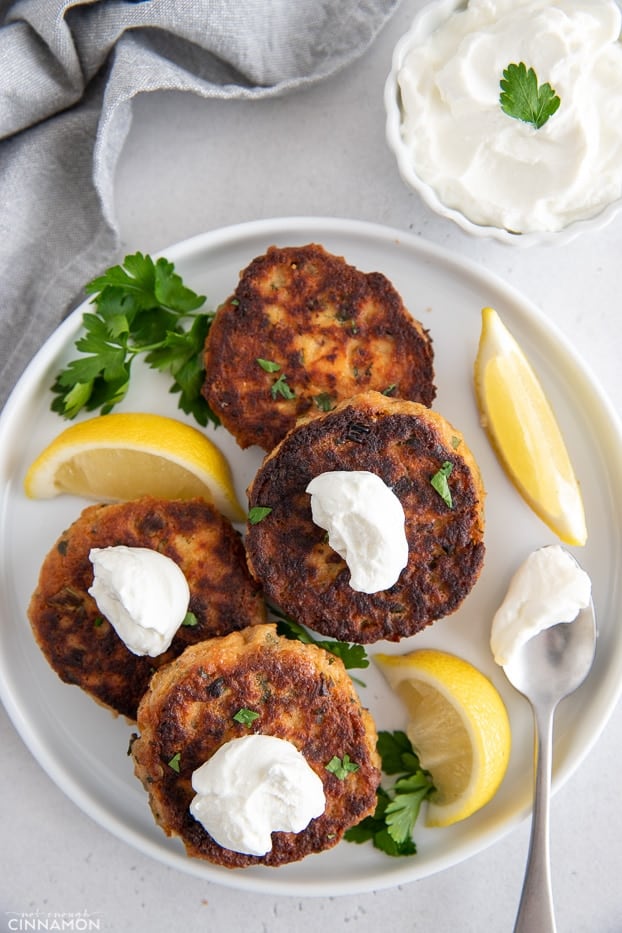 overhead shot of healthy gluten-free salmon patties served with dollops of sour cream and lemon wedges