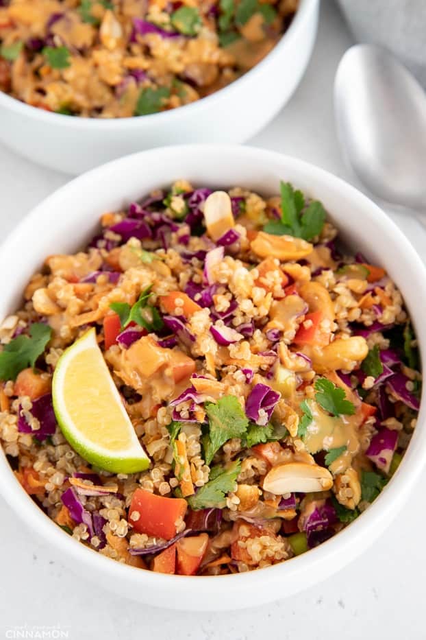 close-up of a bowl of Thai Quinoa Salad decorated with lime slices and cilantro and drizzled with Peanut Dressing 
