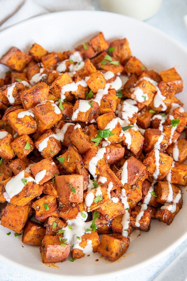 roasted sweet potato cubes on a white plate drizzled with tahini sauce 