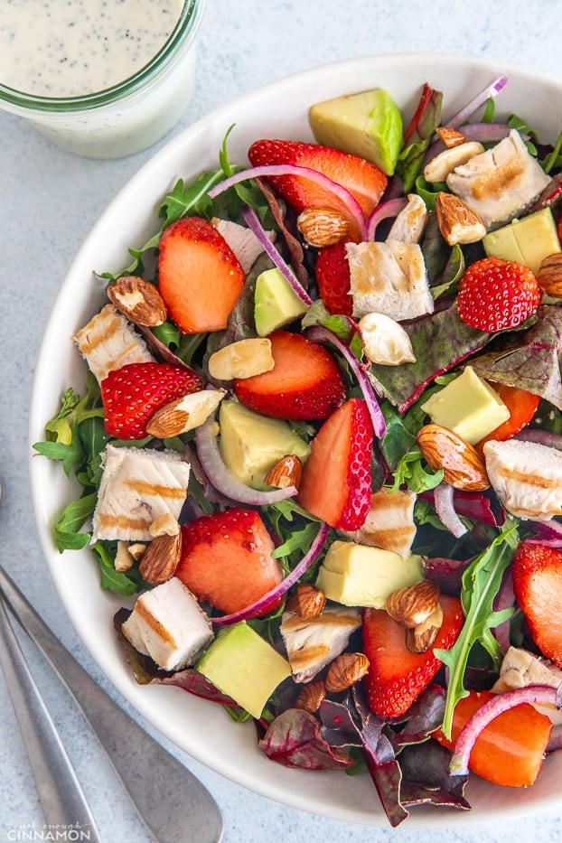 overhead shot of a big bowl with strawberry chicken salad with almonds and avocados with creamy poppy seed dressing in the background