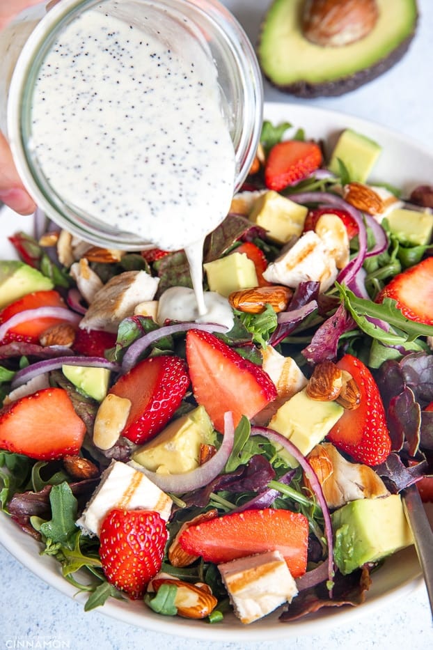 creamy lemon poppy seed dressing being poured on top of healthy strawberry chicken salad