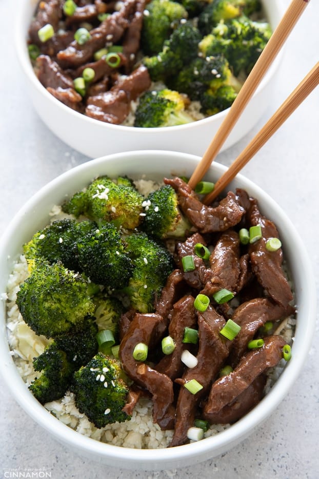 a bowl of Mongolian Beef and Broccoli served over cauliflower rice with chopsticks on the side