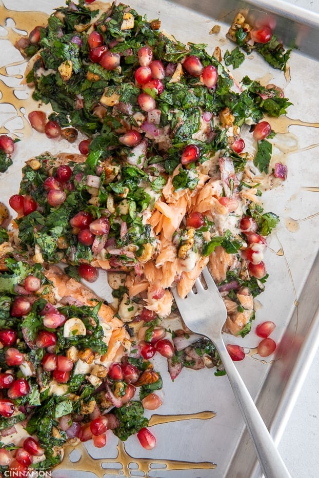a fork tucking into a baked salmon fillet covered with herbs and pomegranate seeds