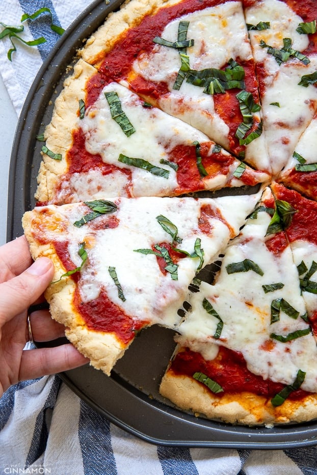 a hand taking a cheesy slice of gluten-free paleo pizza Margherita 