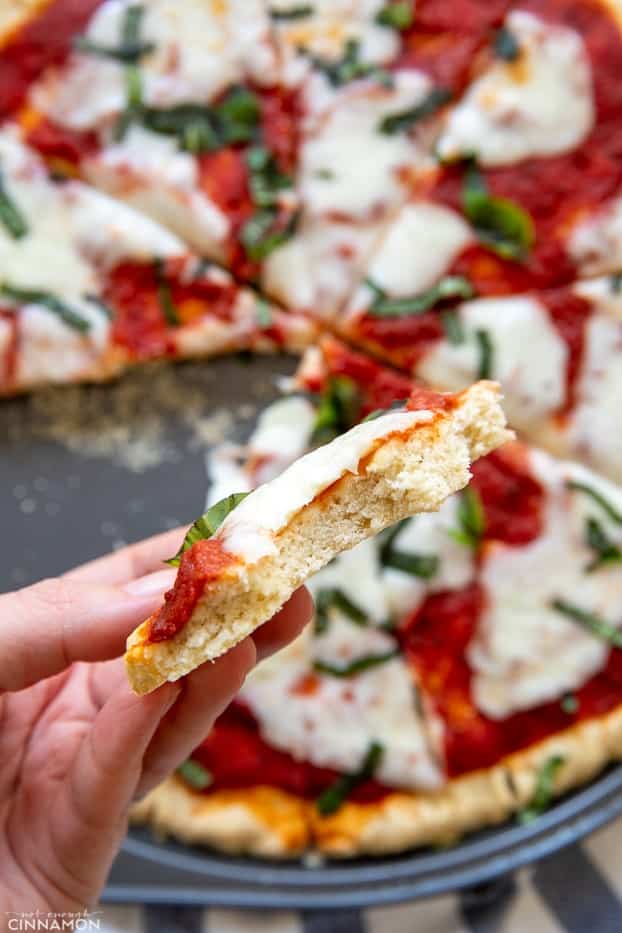 a hand holding a cheesy slice of paleo Pizza Margherita 