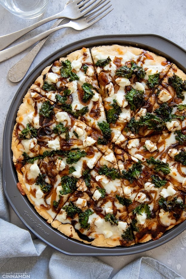 overhead shot of a gluten-free kale pizza with goat cheese, balsamic drizzle and caramelized onion