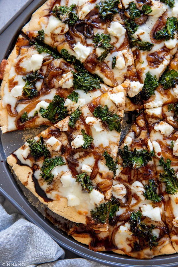 close-uo overhead shot of a goat cheese and kale pizza drizzled with balsamic reduction 