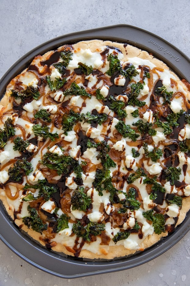 overhead shot of a kale pizza with caramelized onions and goat cheese drizzled with balsamic reduction 